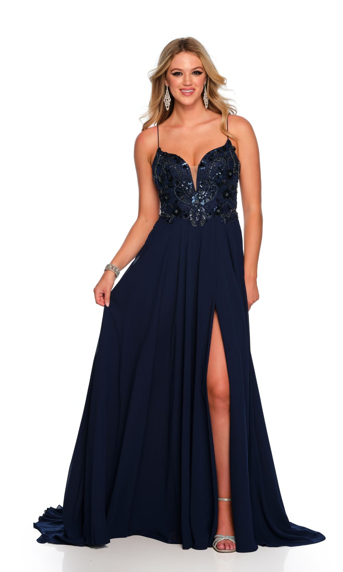 A woman smiles while wearing the Dave and Johnny Navy Blue Long Formal Dress 11241, which features thin straps, a sequin-embellished bodice, high slit, and is paired with silver high-heeled sandals.